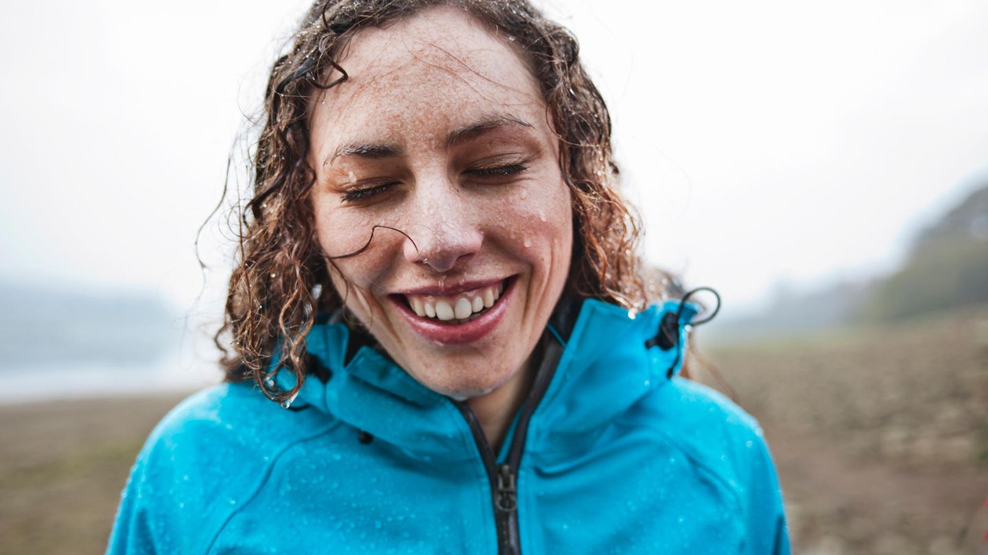 Frau mit nassen Haaren und blauer Jacke lacht im Regen