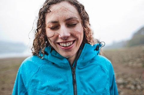 Frau mit nassen Haaren und blauer Jacke lacht im Regen