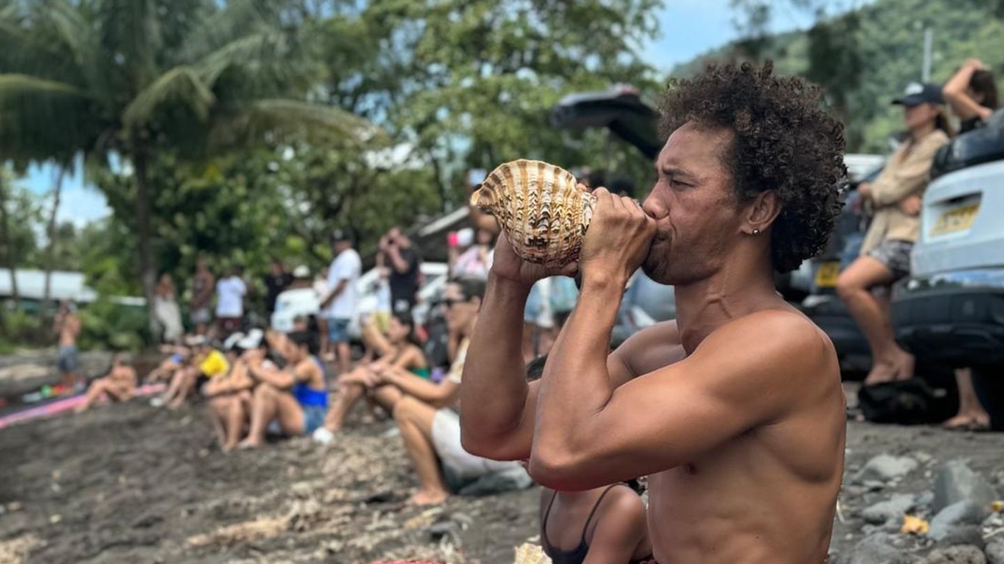 Ein Mann bläst am Strand von Teahupoo in ein Schneckenhorn