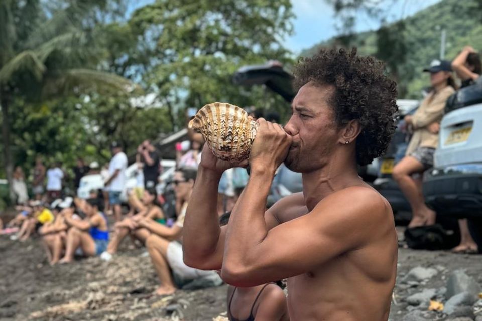 Ein Mann bläst am Strand von Teahupoo in ein Schneckenhorn