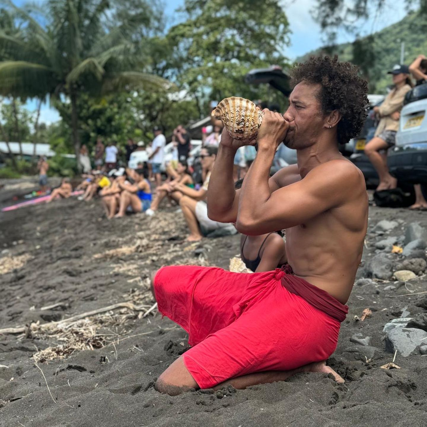 Ein Mann bläst am Strand von Teahupoo in ein Schneckenhorn