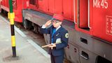 Vor einer Diesellok steht ein Junge mit Kelle in Bahnuniform und salutiert