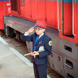 Vor einer Diesellok steht ein Junge mit Kelle in Bahnuniform und salutiert
