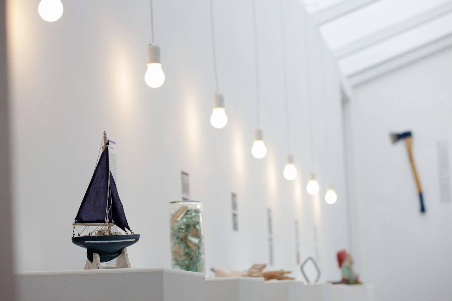 Man sieht Ausstellungsstücke, ein kleines Kindersegelboot, an der Wand hängt eine Axt.