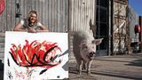 Junge Frau vor Scheunentor aus Holz, neben ihr ein großes Schwein und ein Bild.