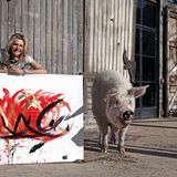 Junge Frau vor Scheunentor aus Holz, neben ihr ein großes Schwein und ein Bild.