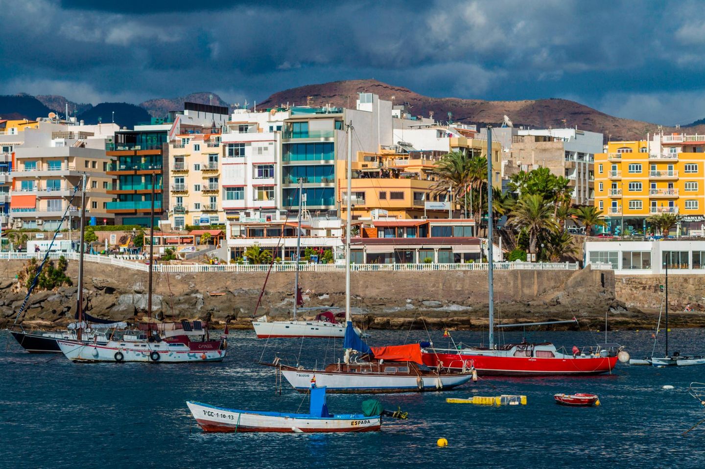 Hafenpromenade mit Häuserfront vor Bergen, davor Schiffe im Wasser