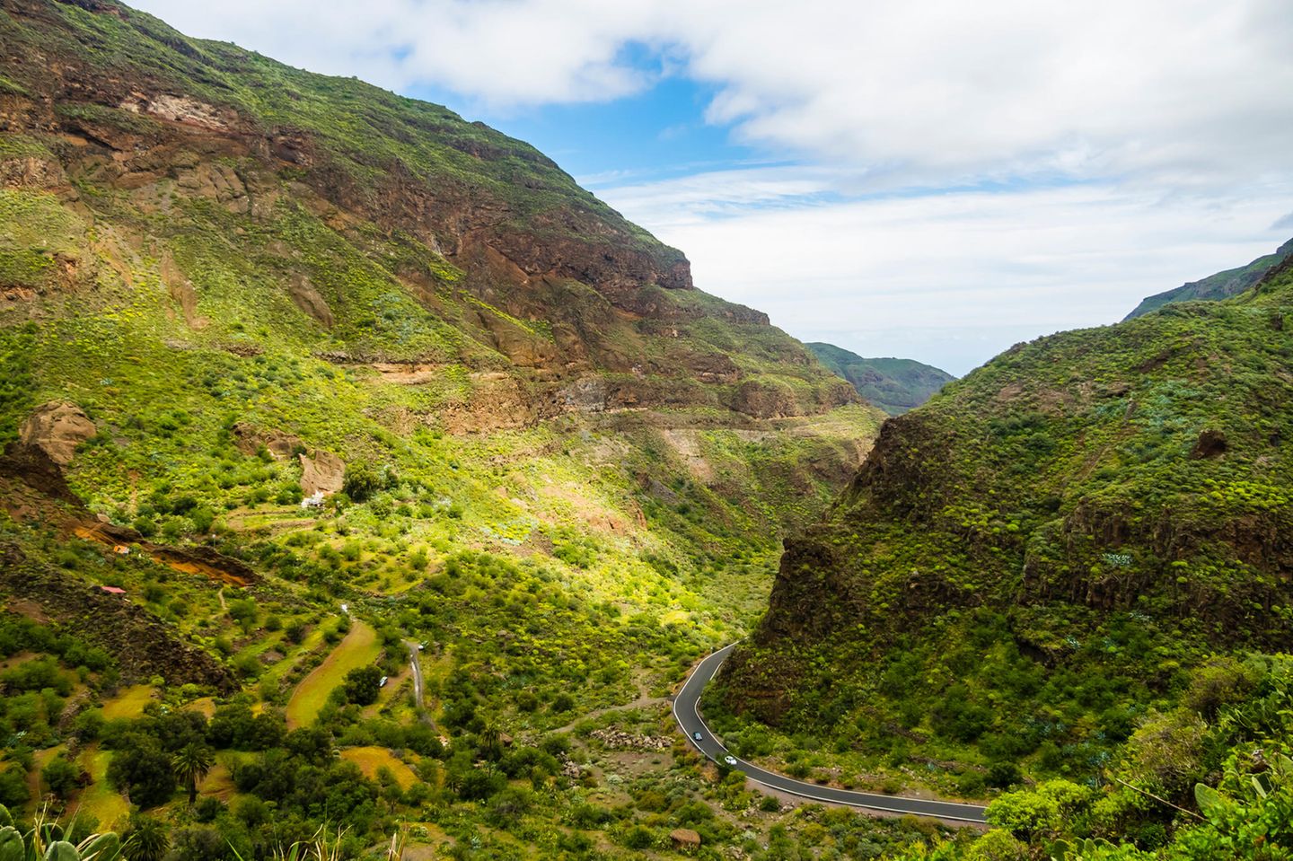 Grüne Berglandschaft mit einem Tal, durch das eine schmale Straße führt