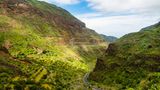 Grüne Berglandschaft mit einem Tal, durch das eine schmale Straße führt