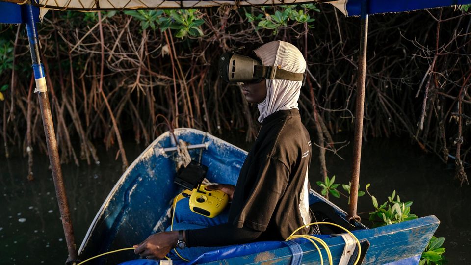 Rokhaya Diagne sitzt in einem Boot und steuert eine Drohne