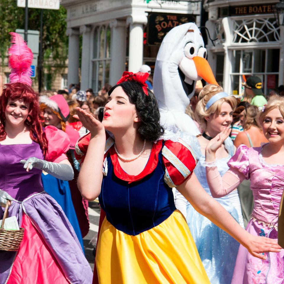 Frauen in Disney-Prinzessinnen-Kostümen, im Vordergrund Schneewittchen, die einen Luftkuss zur Seite wirft