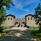 Steinbau gesäumt von Bäumen mit zwei Eingangstoren, dazwischen eine römische STatue