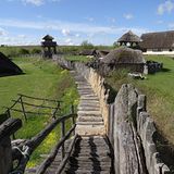 schmaler Holzweg führt über Wiese vorbei an mehreren Holzhütten