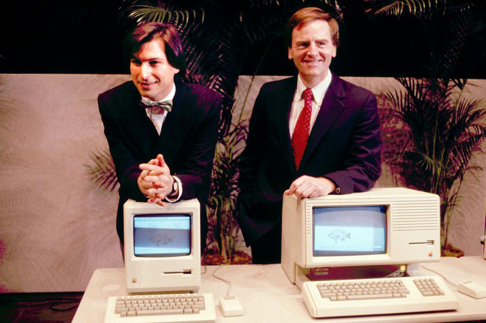 Steve Jobs lehnt auf dem Macintosh PC, daneben John Sculley hinter einem anderen Modell  1.4076