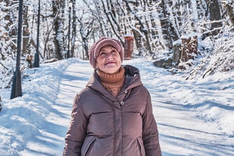 Ältere lächelnde Frau auf einem verschneiten Waldweg