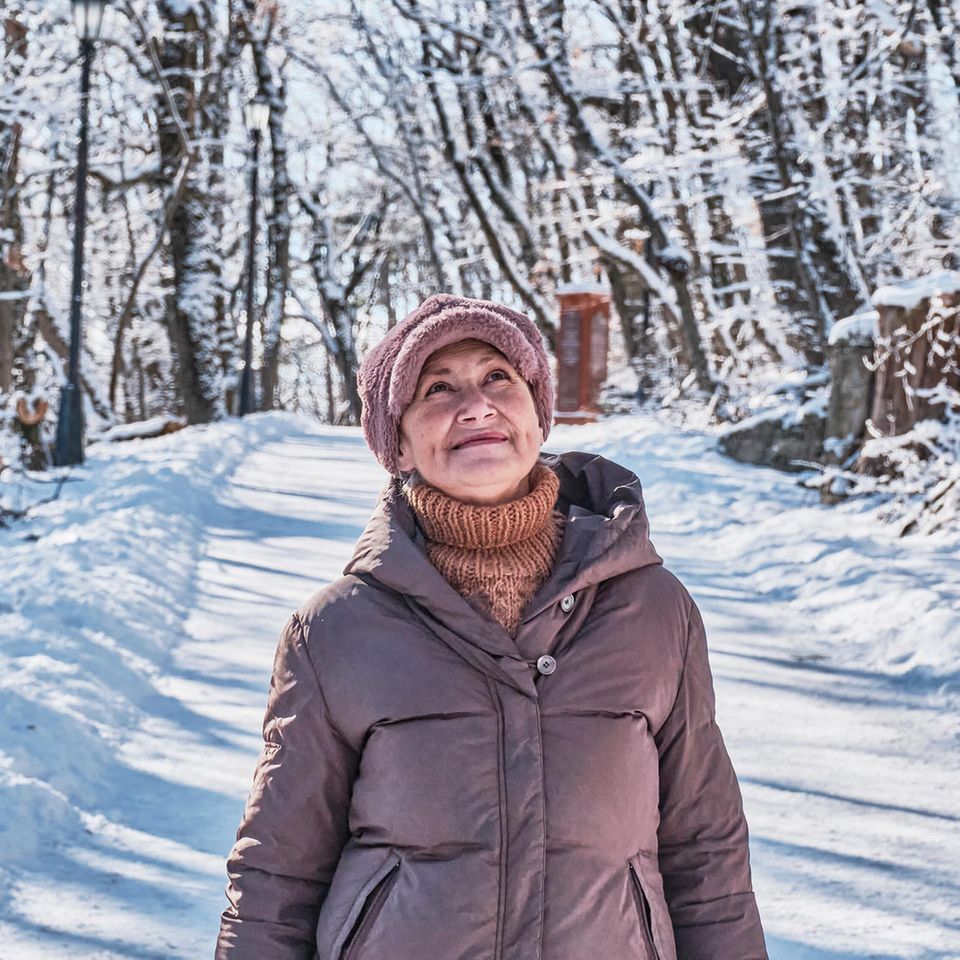 Ältere lächelnde Frau auf einem verschneiten Waldweg