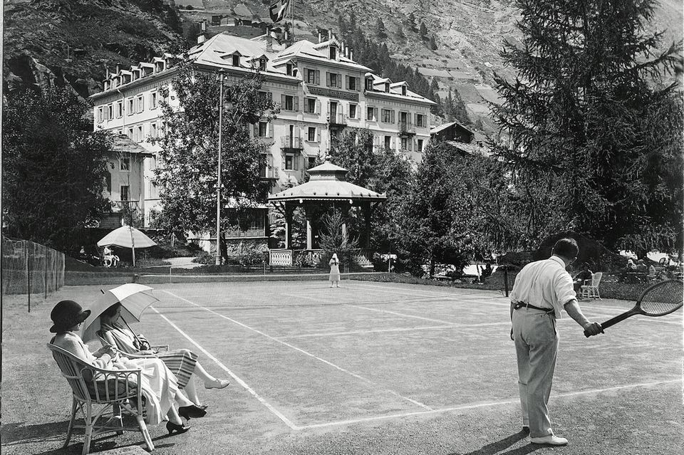 Tennisplatz und Hotel im Hintergrund, umgeben von ein paar Bäumen  1.3394