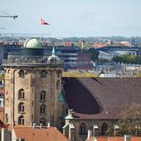 Blick über die Stadt mit einem runden Turm im Zentrum auf dessen Dach sich Menschen tummeln
