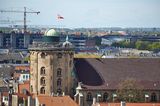 Blick über die Stadt mit einem runden Turm im Zentrum auf dessen Dach sich Menschen tummeln