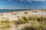 Meer und Sandstrand bei Sonnenschein, einige Menschen auf Decken und im Wasser