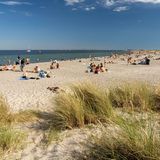 Meer und Sandstrand bei Sonnenschein, einige Menschen auf Decken und im Wasser