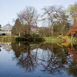 Teich gesäumt von fast kahlen Bäumen, am Ufer eine gläsernes Gebäude