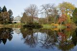 Teich gesäumt von fast kahlen Bäumen, am Ufer eine gläsernes Gebäude