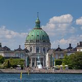 Kirche mit grünem Dach umgeben von Häusern, davor Treppen am Fluss