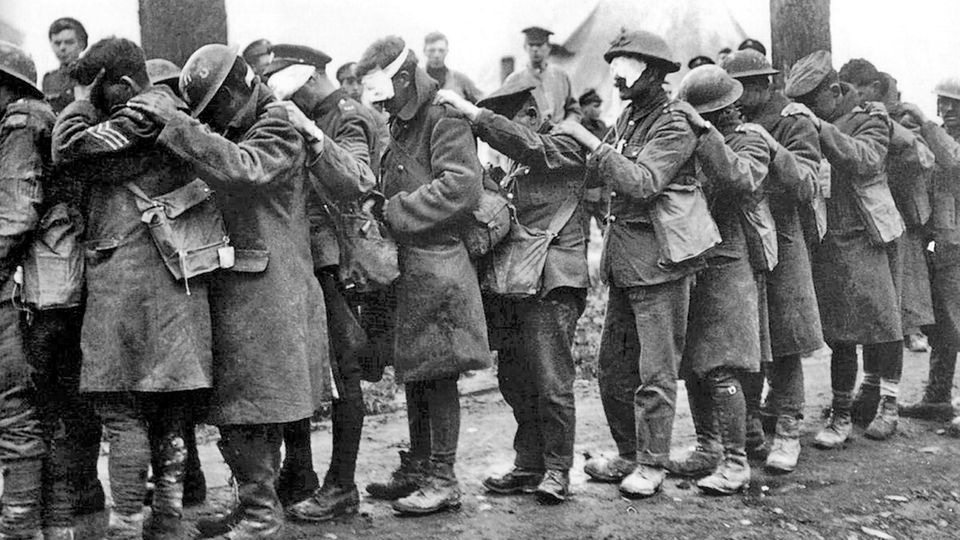 Männer in Uniform, teils mit Helmen, stehen hintereinander in einer Reihe, alle haben die Augen bedeckt Männer in Uniform, teils mit Helmen, stehen hintereinander in einer Reihe, alle haben die Augen bedeckt