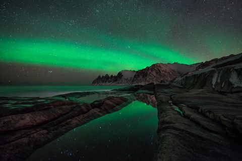 Nordlichter und Sternenhimmel über Felsen und Meer