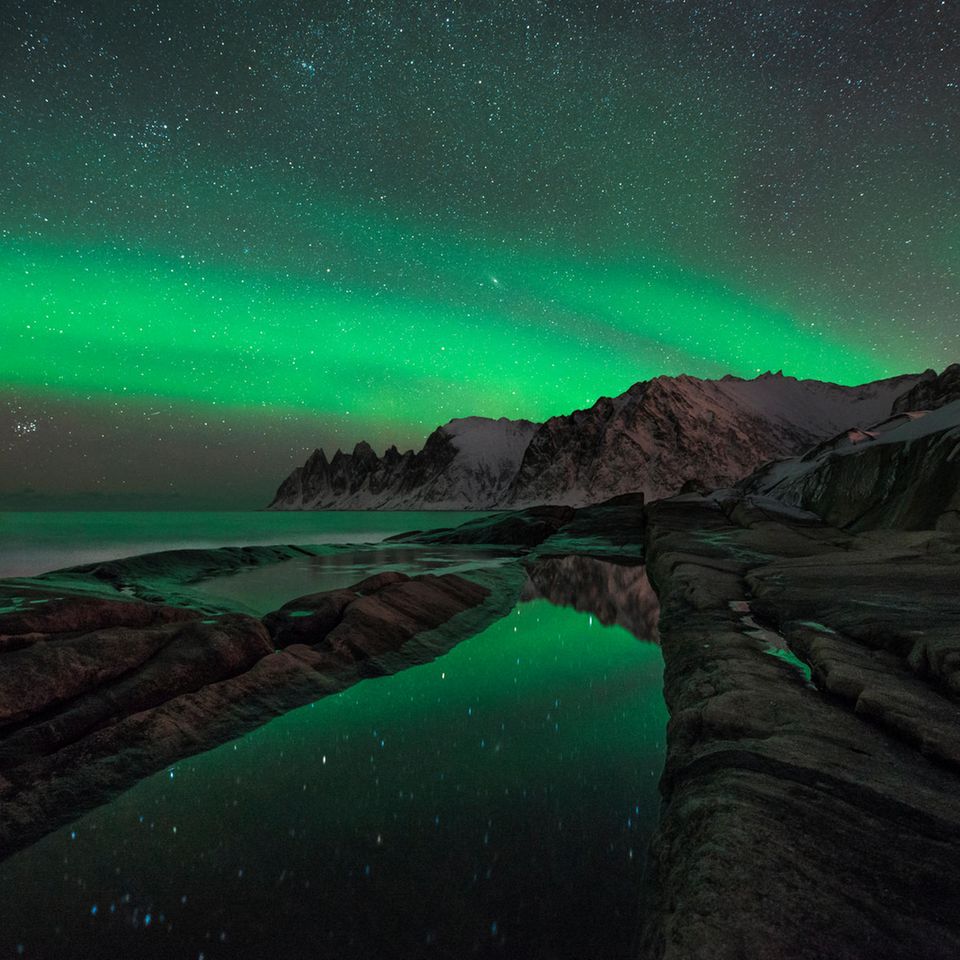 Nordlichter und Sternenhimmel über Felsen und Meer
