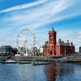 Großes rotes Gebäude, Riesenrad und Wohnhäuser vor einem Fluss mit Steg