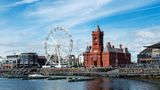 Großes rotes Gebäude, Riesenrad und Wohnhäuser vor einem Fluss mit Steg
