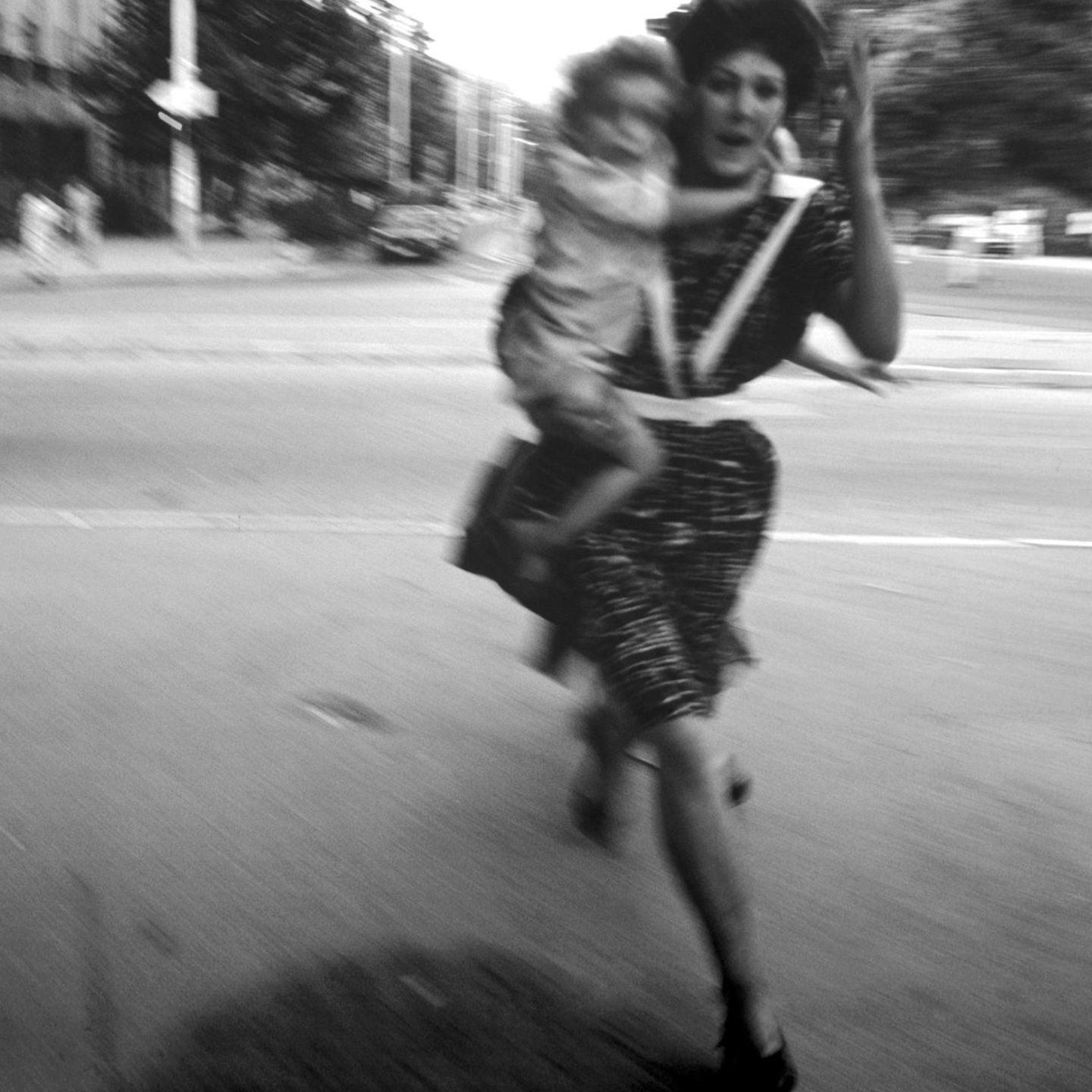 Eine Frau rennt mit einem Kind auf dem Arm über eine Straße