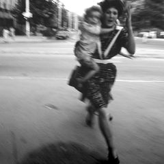 Eine Frau rennt mit einem Kind auf dem Arm über eine Straße