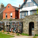 Steinmauer mit Durchganz zu Wohnhäusern, volle Bücherregale vor der Mauer