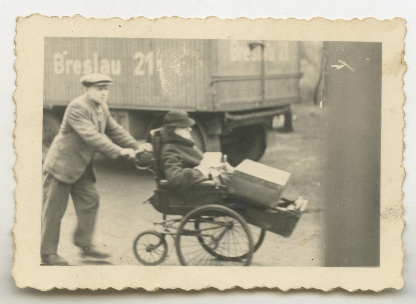 Mann schiebt Frau im Rollstuhl, Lastwagen im Hintergrund