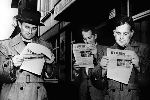 Lohn auch im Krankheitsfall Männer lesen eine Streikzeitung