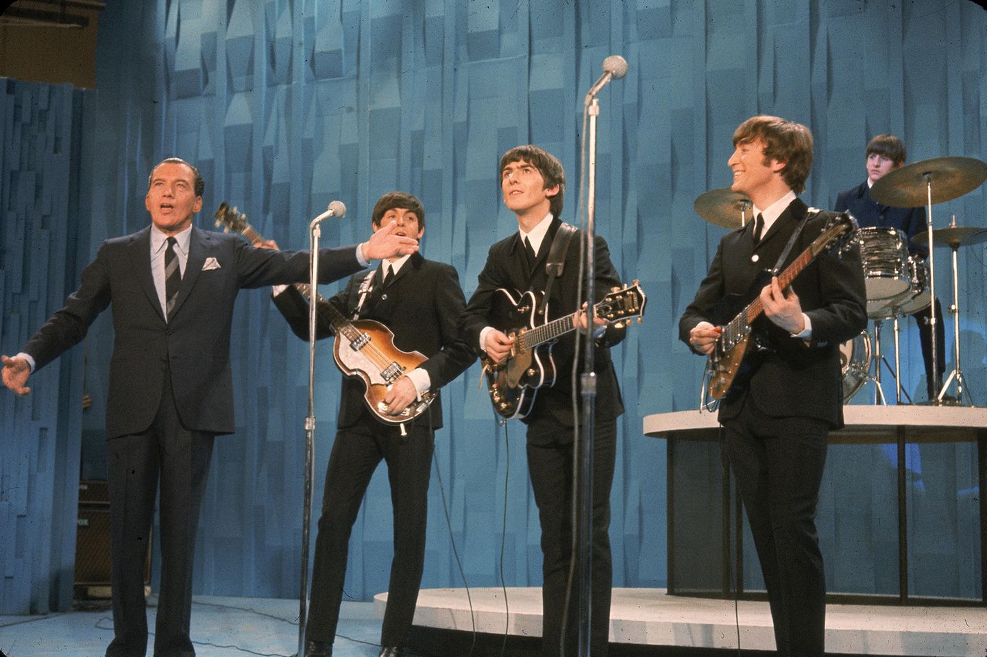 Die Nation schaut zu Die Beatles mit Instrumenten auf einer Bühne, neben ihnen Ed Sullivan