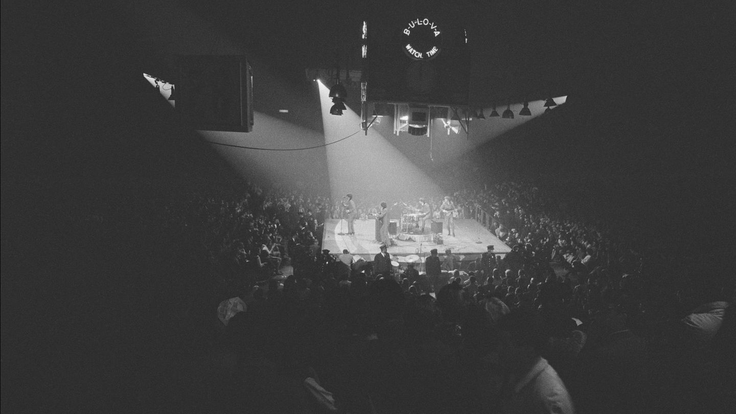 Die Beatles bei einem Live-Konzert auf einer Bühne, umringt von Fans