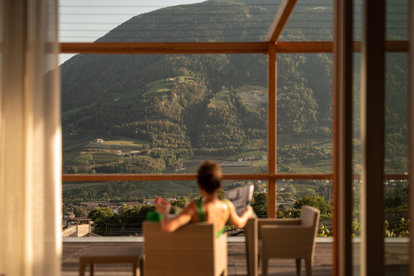 Pergola Residence, Algund: Panoramafenster zum Davonschmelzen Frau blickt auf bewaldete Berge durch Fensterfront