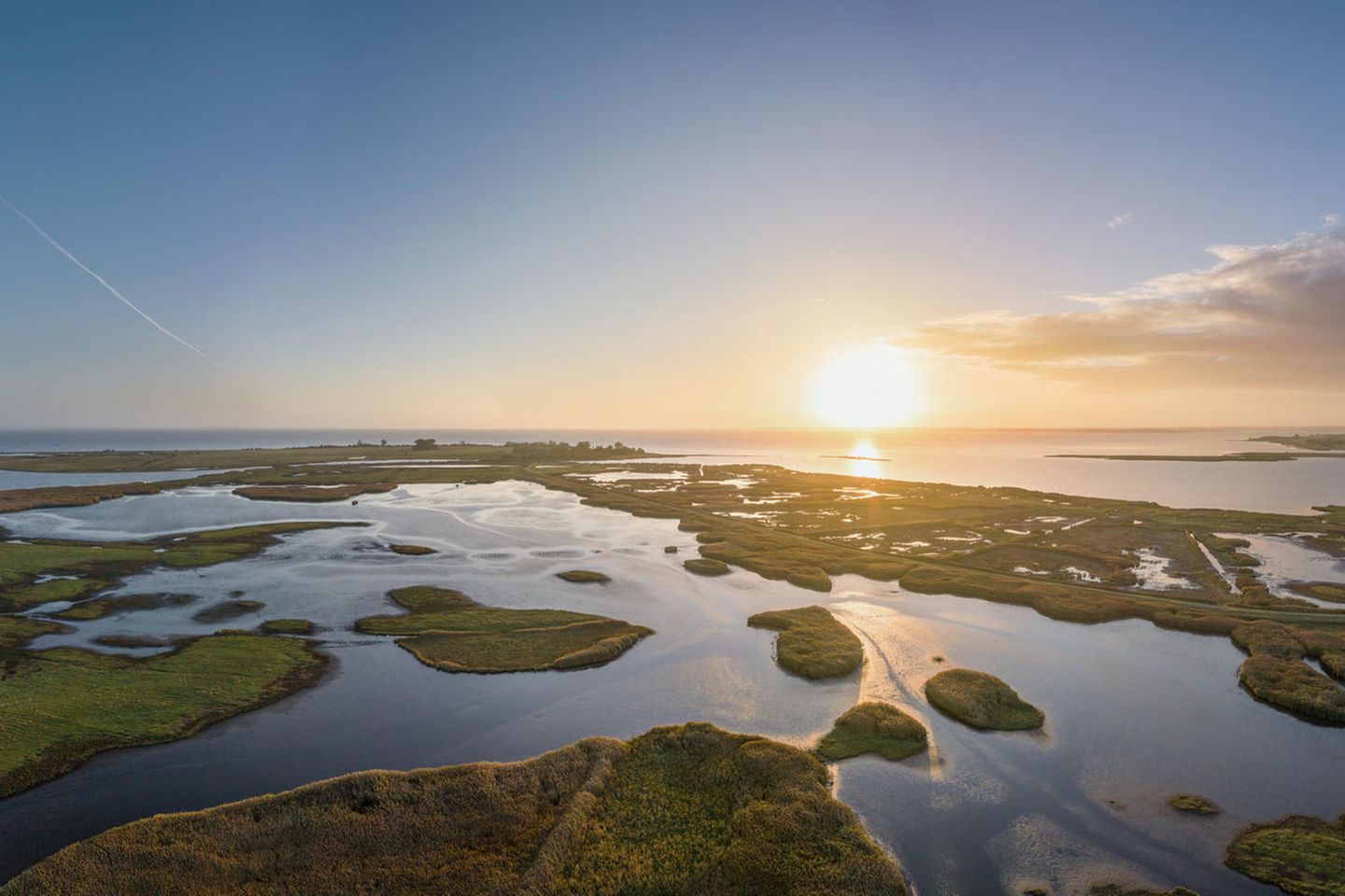 Luftaufnahme von Wasserflächen mit Grasinseln, dahinter die Ostsee