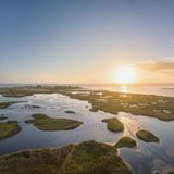 Luftaufnahme von Wasserflächen mit Grasinseln, dahinter die Ostsee