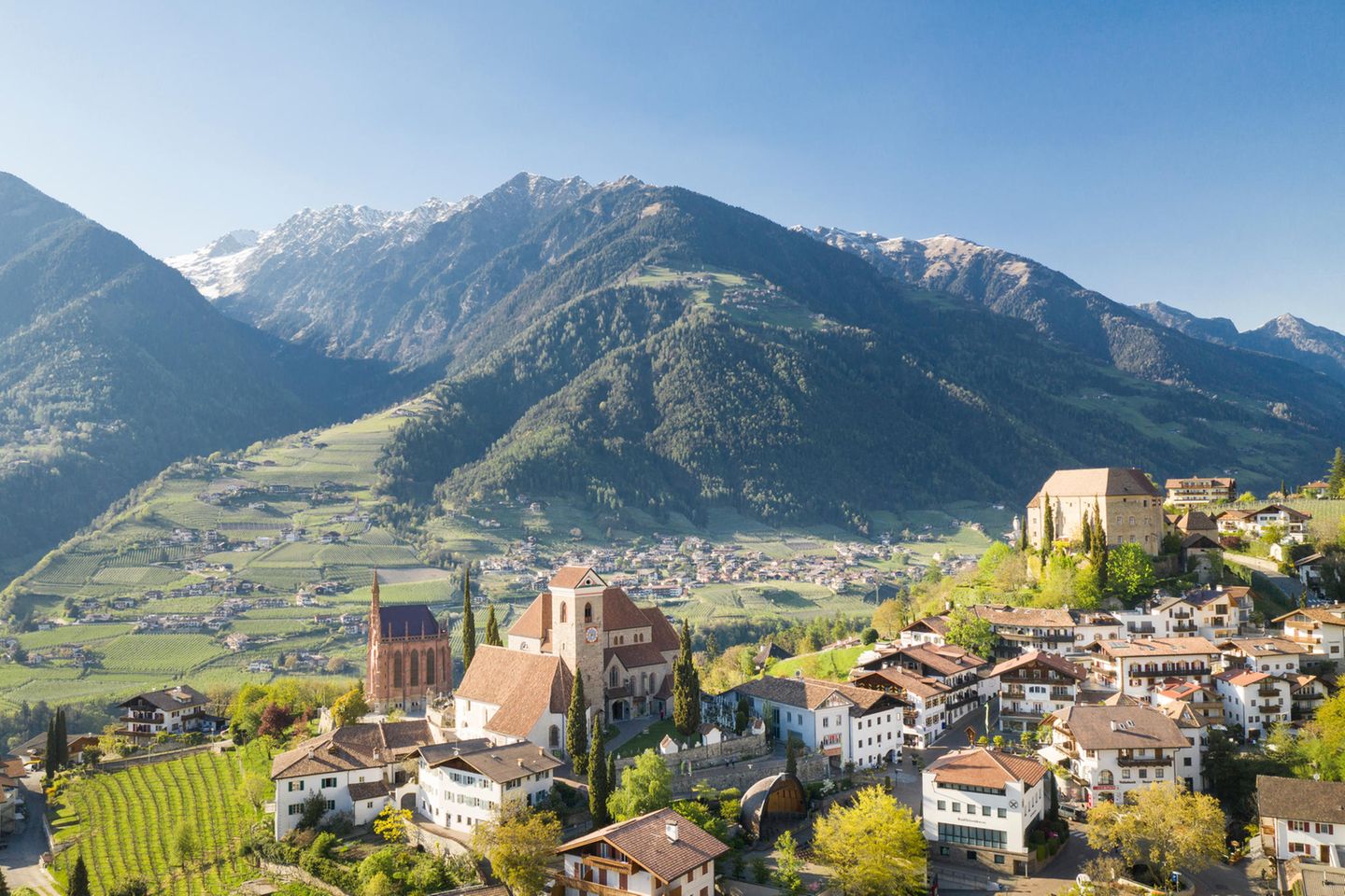 Blick über Dorf mit Kirche, dahinter grüne Berge