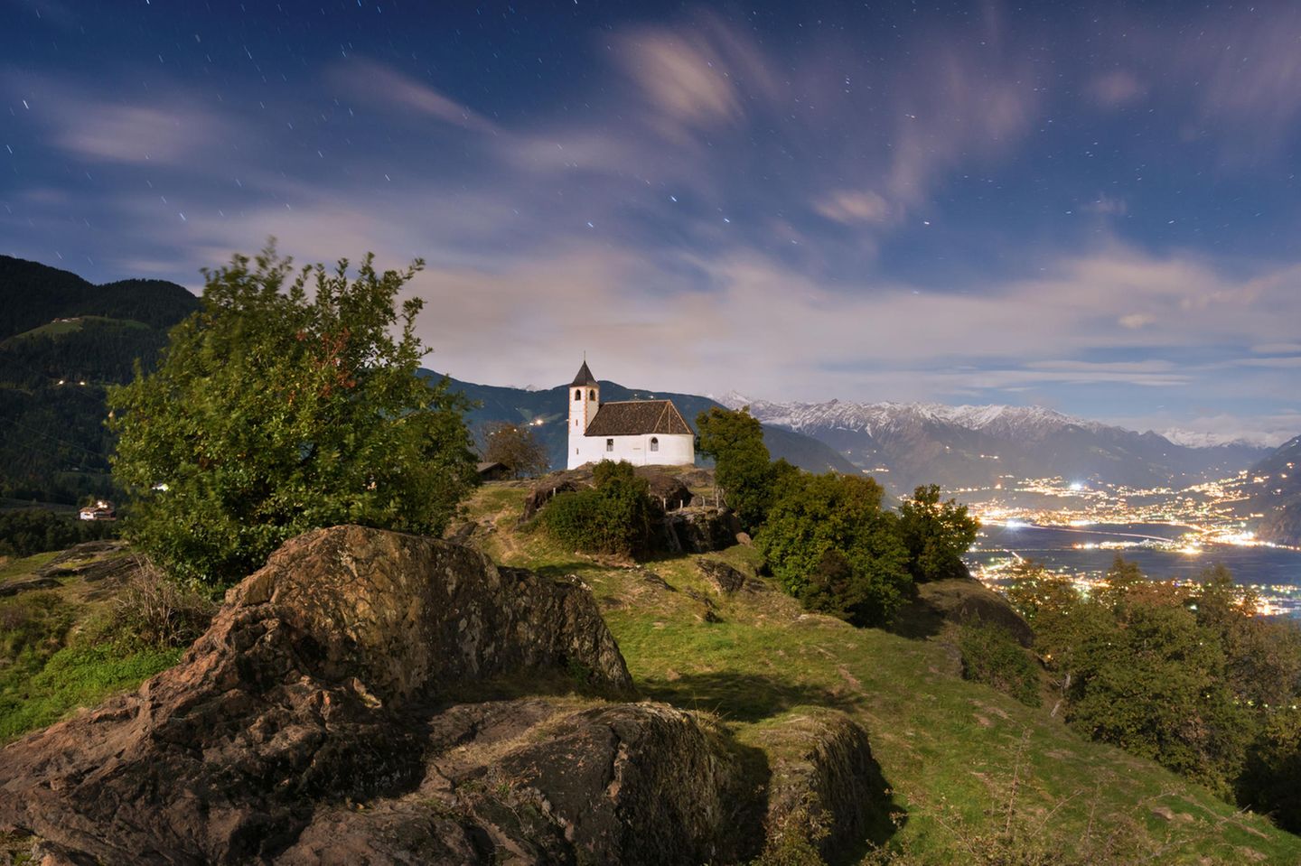Kirche auf Berg, dahinter Berge und Nachthimmel, Felsbrocken im Vordergrund