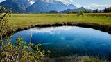 Teich umgeben von Wiese mit Berglandschaft im Hintergrund