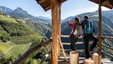 Zwei Wandernde genießen den Ausblick aus einer Holzhütte auf bergige Landschaft