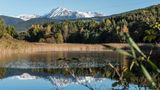 Wald und Berge im Hintergrund spiegeln sich in ruhigem Wasser