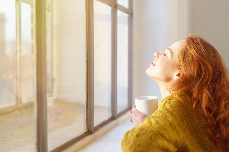 eine Frau entspannt mit einem Getränk in der Hand am Fenster