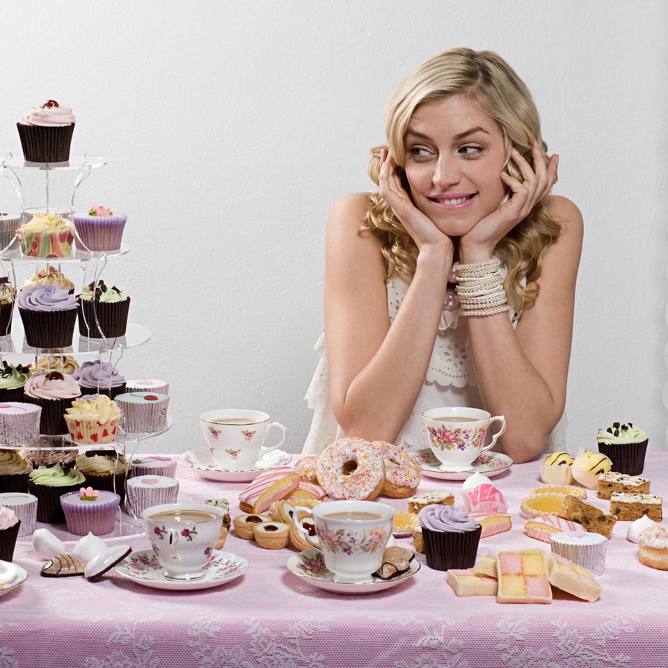 Frau an einem Tisch, umgeben von Cupcakes und anderen Desserts